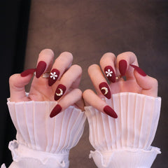 Uñas postizas en rojo mate almendra medio con adornos de flores y lunas
